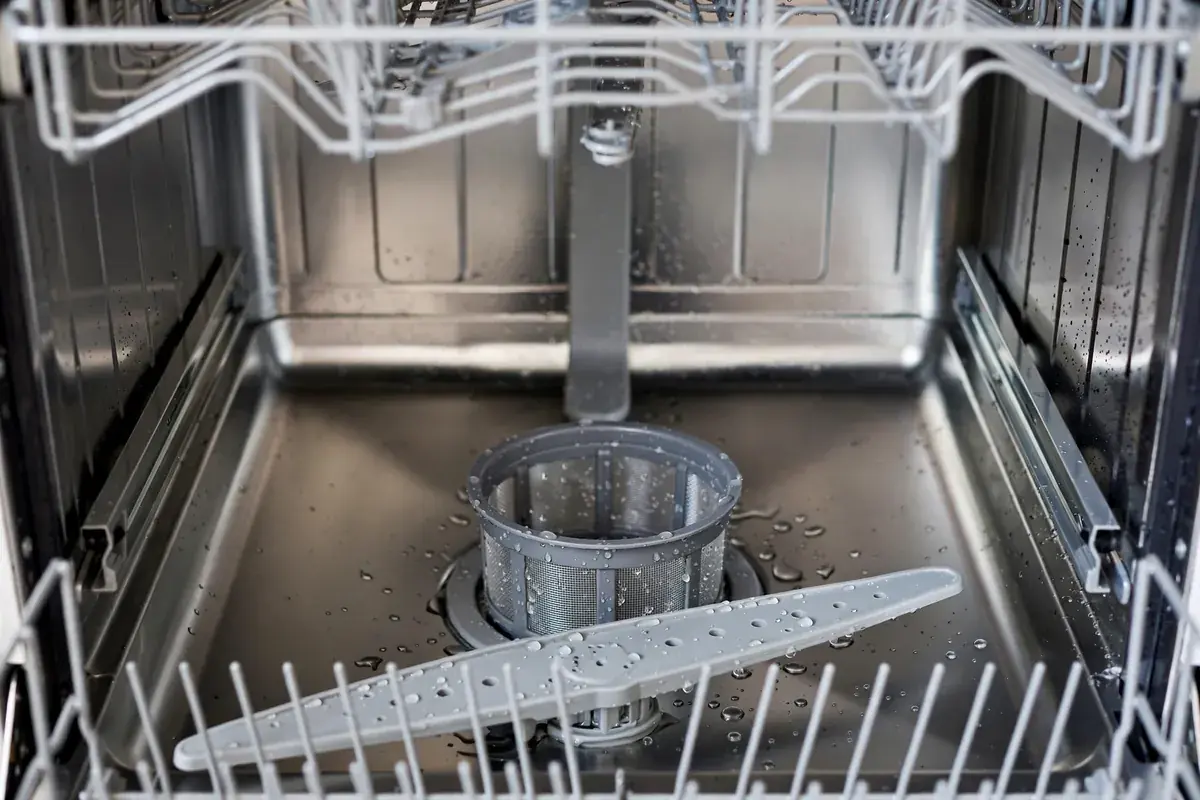 Dishwasher filter and spray arm seen close up inside a clean stainless tub