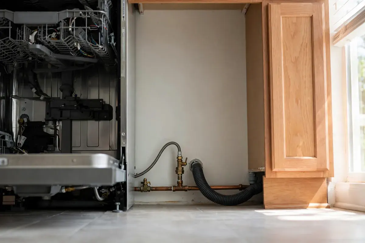 Base of a kitchen dishwasher with the kick panel off showing hoses and connections