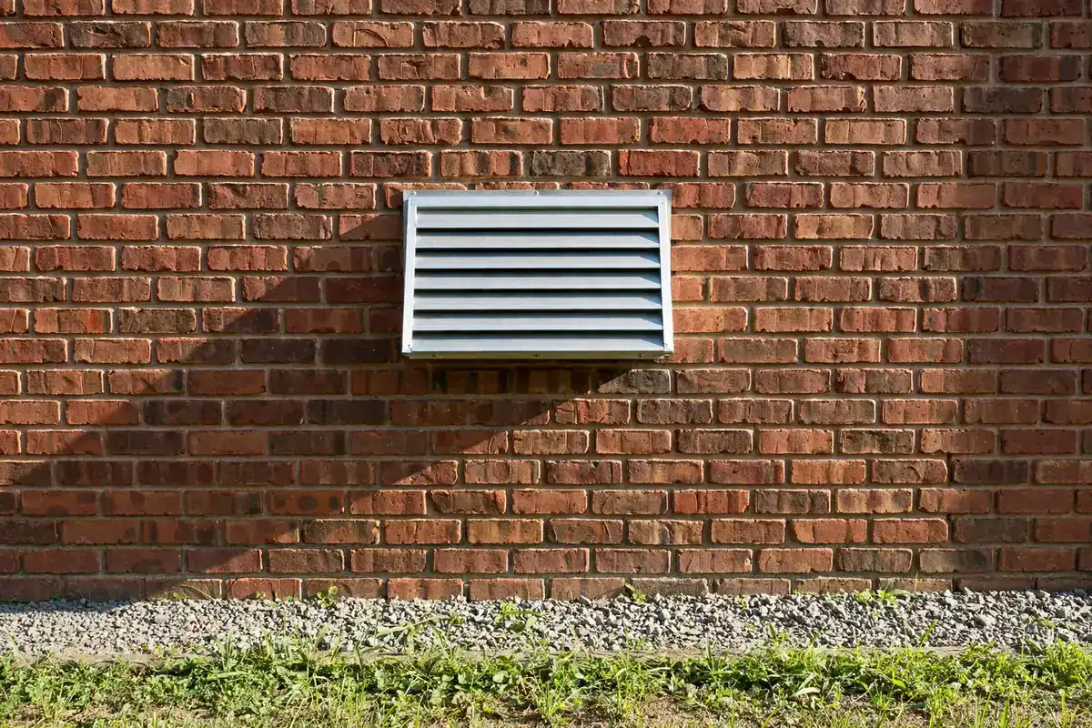 Outside brick wall with a dryer vent hood and a clear patch of ground below