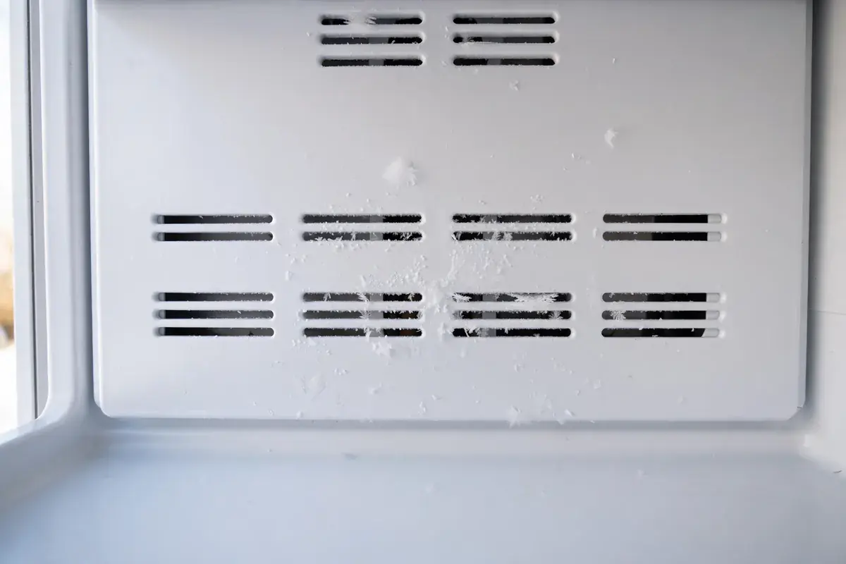 Refrigerator back wall air vent slots with light frost on the panel